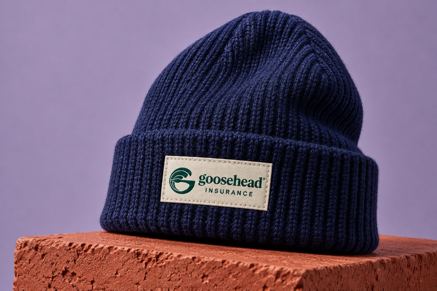 A navy knit beanie with a small branded woven patch on a terracotta plinth.